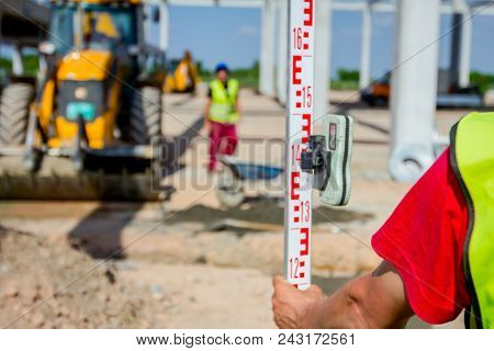 Construction Worker Is Holding Leveling Rod To Help Surveyor, Geodesist To Measure Position, Depth.