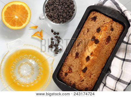 Flat Lay Image Of Chocolate And Orange Cake In A Baking Tin With Choc Chips By The Side  Light Backg