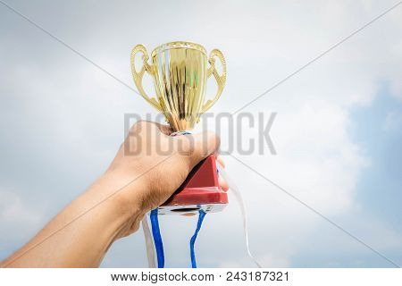 Hand Holding Winner Trophy Cup On Sky Background