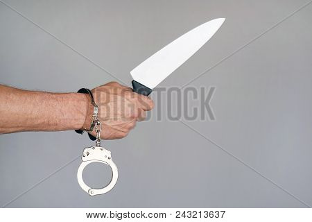 Close-up. Arrested Man Holding A Knife. Handcuffed Hands Isolated On Gray Background. Prisoner Or Ar