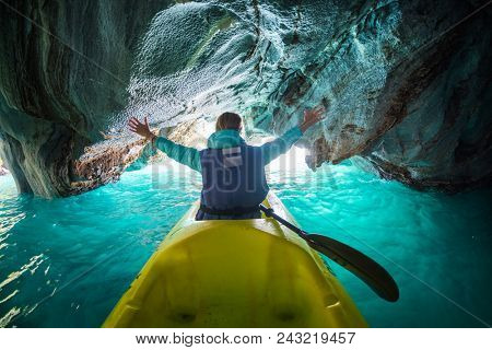 Woman sits in kayak with rised hands inside the Marble Cave on the lake of General Carrera, Chile