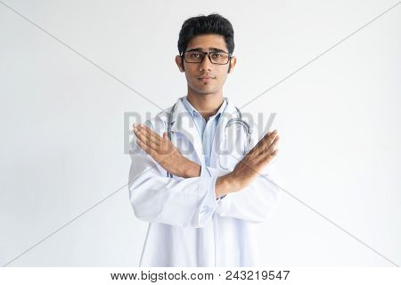 Portrait Of Serious Young Doctor In Glasses Showing Stop Gesture. Indian General Practitioner Wearin
