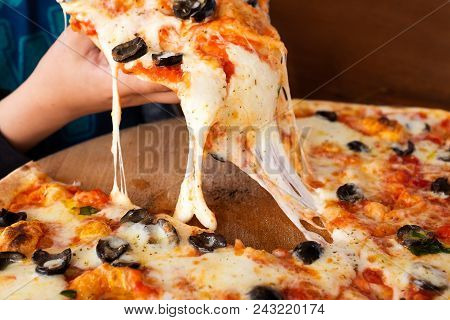 A Child Picking Up A Slice Of Large Margherita Pizza With Black Olives. Melted Cheese.