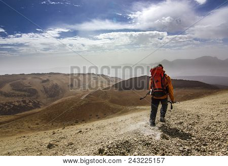 Man With Backpack On Path In Desert Near Neide Volcano On Tenerife Island With Stones And Blue Sky A