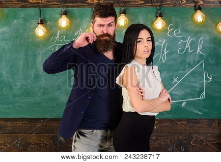 Man With Beard And Sexy Girl Teacher Stand In Classroom, Chalkboard On Background. Teacher And Stric