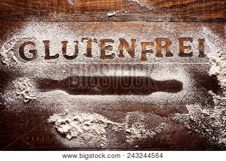 high-angle shot of a wooden table sprinkled with a gluten free flour where you can read the text glutenfrei, gluten free written in german, next to the silhouette of a rolling pin