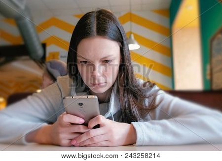 Young Seriously Woman Reading Something On Her Mobile Phone Sitting In Cafe