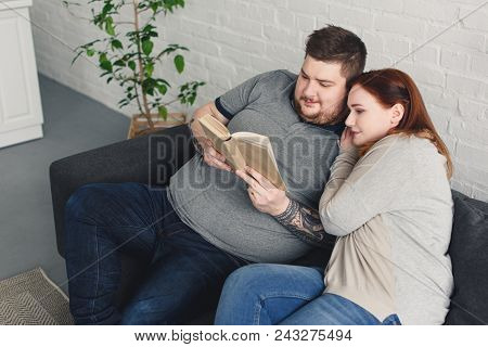 Boyfriend And Girlfriend Reading Book Together On Sofa In Living Room