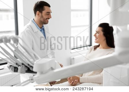 medicine, dentistry and healthcare concept - male dentist talking to female patient and discussing teeth treatment at dental clinic office