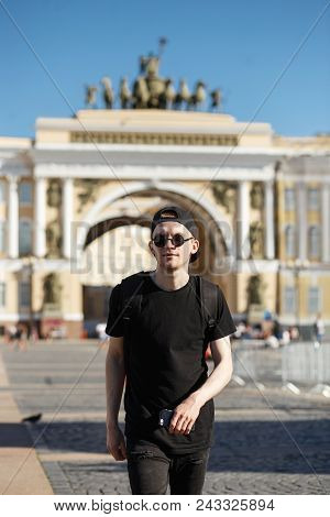 Young Stylish Man Tourist Walking Near General Staff Builsing Arch In The Palace Square In St. Peter