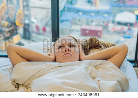 Young Woman Lying On A Bed Covered Her Ears Because Of The Noise. In The Window After The Bed You Ca