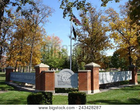 Defiance College Sign And Flag Pole With The United States Of America Flag Surrounded By Fall Foliag