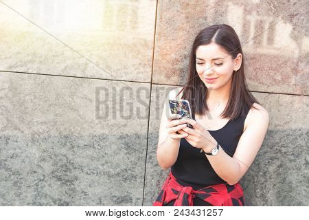 Happy Girl Texting On A Smart Phone Leaned On Marble Wall In City