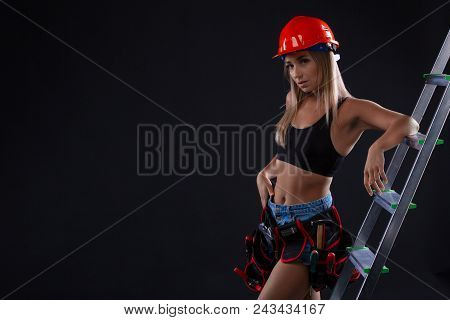 Sexy Construction Female Worker With Ladder On Black Background. Woman Is Wearing A Construction Hel