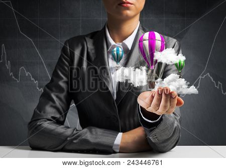 Closeup Of Business Woman In Suit Presenting Flying Aerostate Among Clouds In Her Palm With Business
