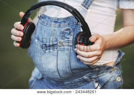 Beautiful Pregnant Woman Holding Headphones On Her Belly. Intrauterine Growth, Pregnancy, Maternity,