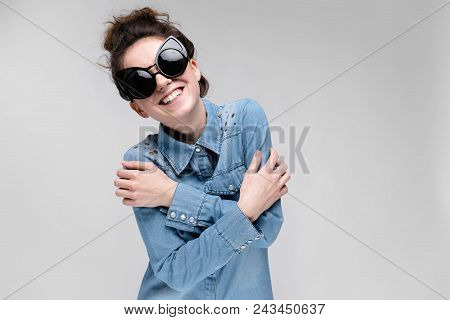 Young Girl In Black Cat Glasses On A Gray Background. Portrait Of A Young Beautiful Girl. Charming G