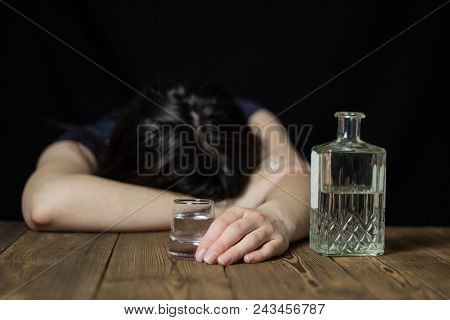 A Drunk Girl Laid Her Head On A Table, In Her Hand A Glass Of Alcohol And A Bottle, A Wooden Table, 