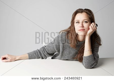 Beautiful Young Brunette Women Sitting At The Table And Smiling Against Empty Gray Background. Studi