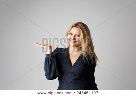 Fashion Photo Of A Beautiful Blonde Woman In A Pretty Dress Posing With Hand Over Gray Empty Backgro