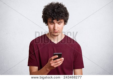 Good Looking Guy With Concetrated Look In Mobile Phone, Recieves Message With Offer To Go Out, Wears