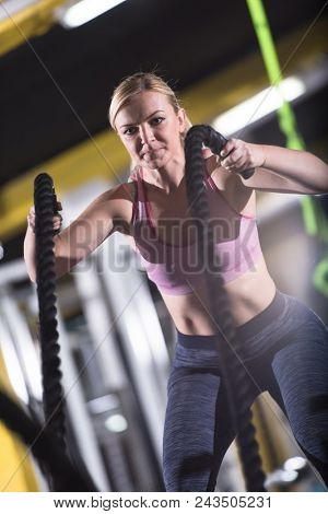 young fit athlete woman working out in functional training gym doing  battle ropes exercise as part of cross fitness training