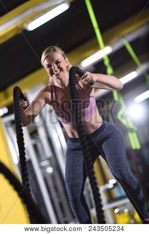 young fit athlete woman working out in functional training gym doing  battle ropes exercise as part of cross fitness training