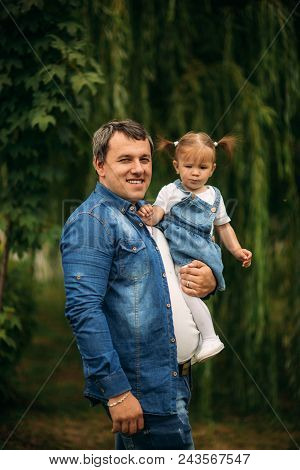 Dad And Daughter Dressed In Jeans Walking In The Pakr And Have Fun.
