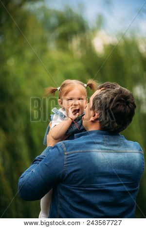 Dad And Daughter Dressed In Jeans Walking In The Pakr And Have Fun.