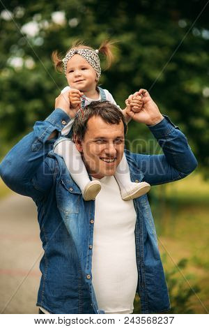 Dad And Daughter Dressed In Jeans Walking In The Pakr And Have Fun.