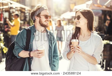 Couple Of Stylish Young Casual Teens With Sunglasses Holding Cups Of Coffee Walking Down The Street 