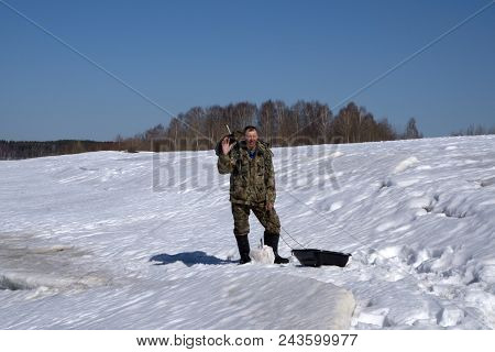 Winter Ice Fishing, A Fisherman In Warm Clothes Fishing In The Hole - Russia Berezniki 7 April 2018