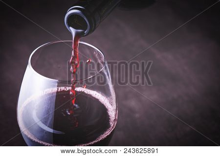 Pouring white wine into the glass against wooden background
