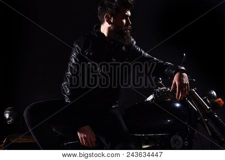 Brutality And Masculine Concept. Man With Beard, Biker In Leather Jacket Lean On Motor Bike In Darkn