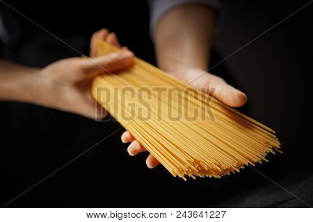 Long raw spaghetti in the women's hands on a dark background. Italian raw food