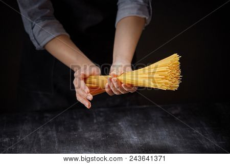 Raw italian pasta in female hands on dark background