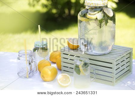 Preparation Of The Lemonade Drink. Lemonade In The Jug And Lemons With Mint On The Table Outdoor