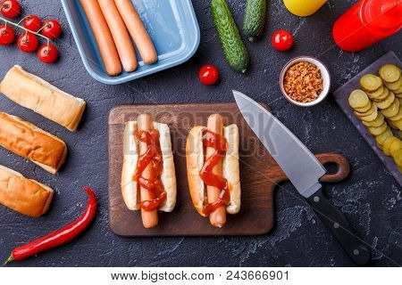 Photo On Top Of Two Hotdogs On Cutting Board On Table With Sausages, Bread, Tomatoes