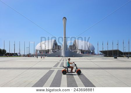 SOCHI, RUSSIA - JUL 09, 2017: Bowl of Olympic flame Firebird and singing Fountain in Olympic park. Symbol of Olympic Games of 2014 in Sochi, woman on moped