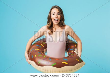 Portrait of an excited girl dressed in swimsuit holding infatable ring isolated over blue background