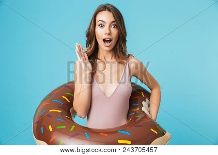 Portrait of an excited girl dressed in swimsuit holding infatable ring isolated over blue background