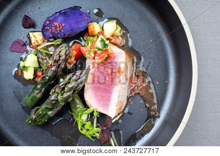 Modern fried tuna fish filet with green asparagus blue potatoes und vegetable chili relish as top view on a plate with copy space right