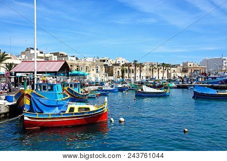 Marsaxlokk, Malta - April 1, 2017 - Traditional Maltese Dghajsa Fishing Boats In The Harbour With Wa
