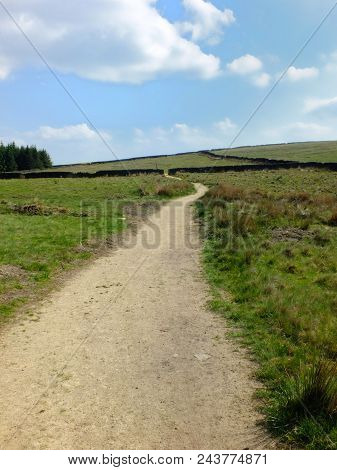 A Long Winding Footpath Running Into The Distance In Stoodley Moor In Yorkshire With Fields And Farm