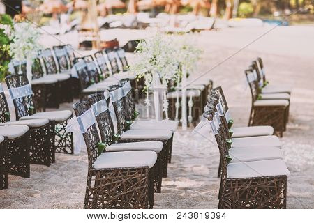 A Group Of Weave Wooden Chairs With White Sash Decoration And Cone Of Rose Petals Arrangement For Be