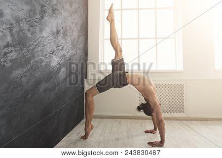 Young Flexible Man Practicing Yoga, Making Corner Stretching Exercise At Wall In Gym, Copy Space