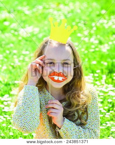Girl Sits On Grass At Grassplot, Green Background. Child Posing With Cardboard Smiling Lips And Crow