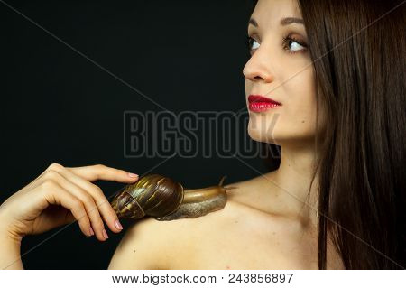 Portrait Of Attractive Young Girl With Big Snail On Shoulder On Black Background In Studio.