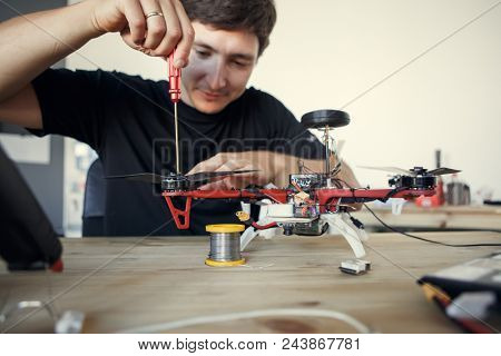 Photo of engineer with screwdriver fixing square copter at table