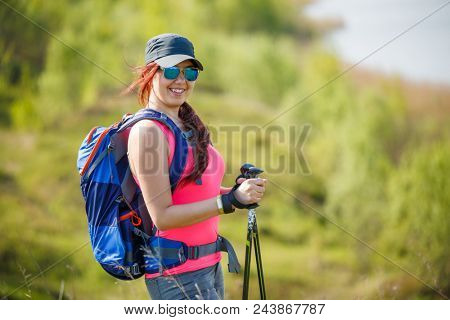 Image of sports girl with walking sticks on background of lake and green vegetation